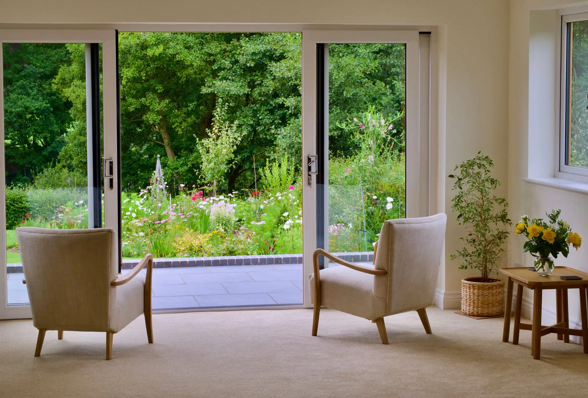 Garden lounge with two armchairs facing open sliding glass doors onto a planted garden
