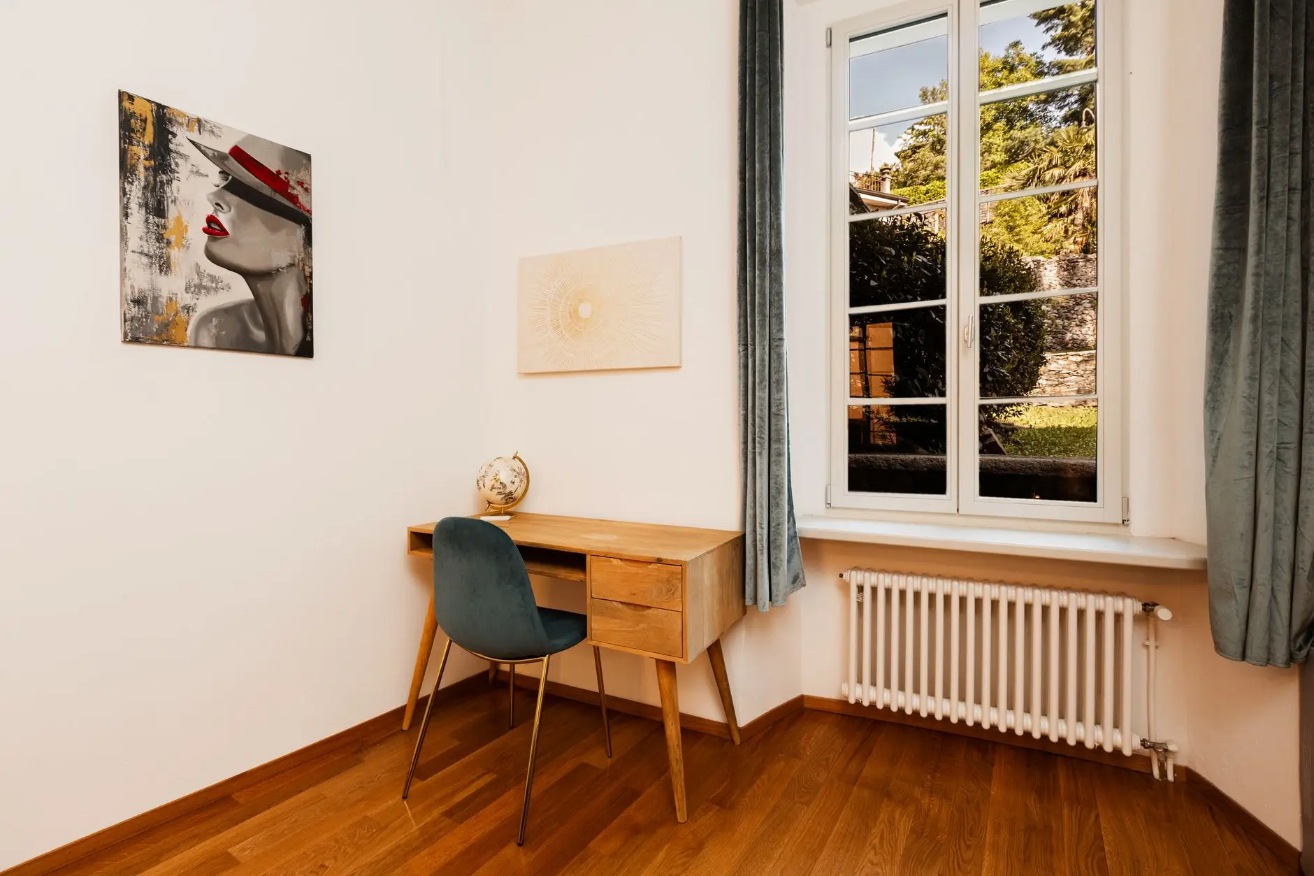 Simple desk and chair beside a tall window, with a white radiator underneath and wooden flooring