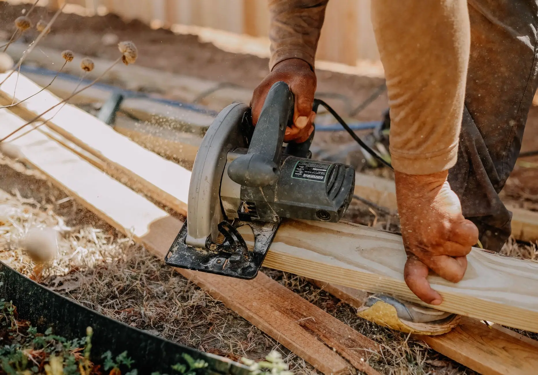 Carpenter cutting a timber board with a circular saw outdoors