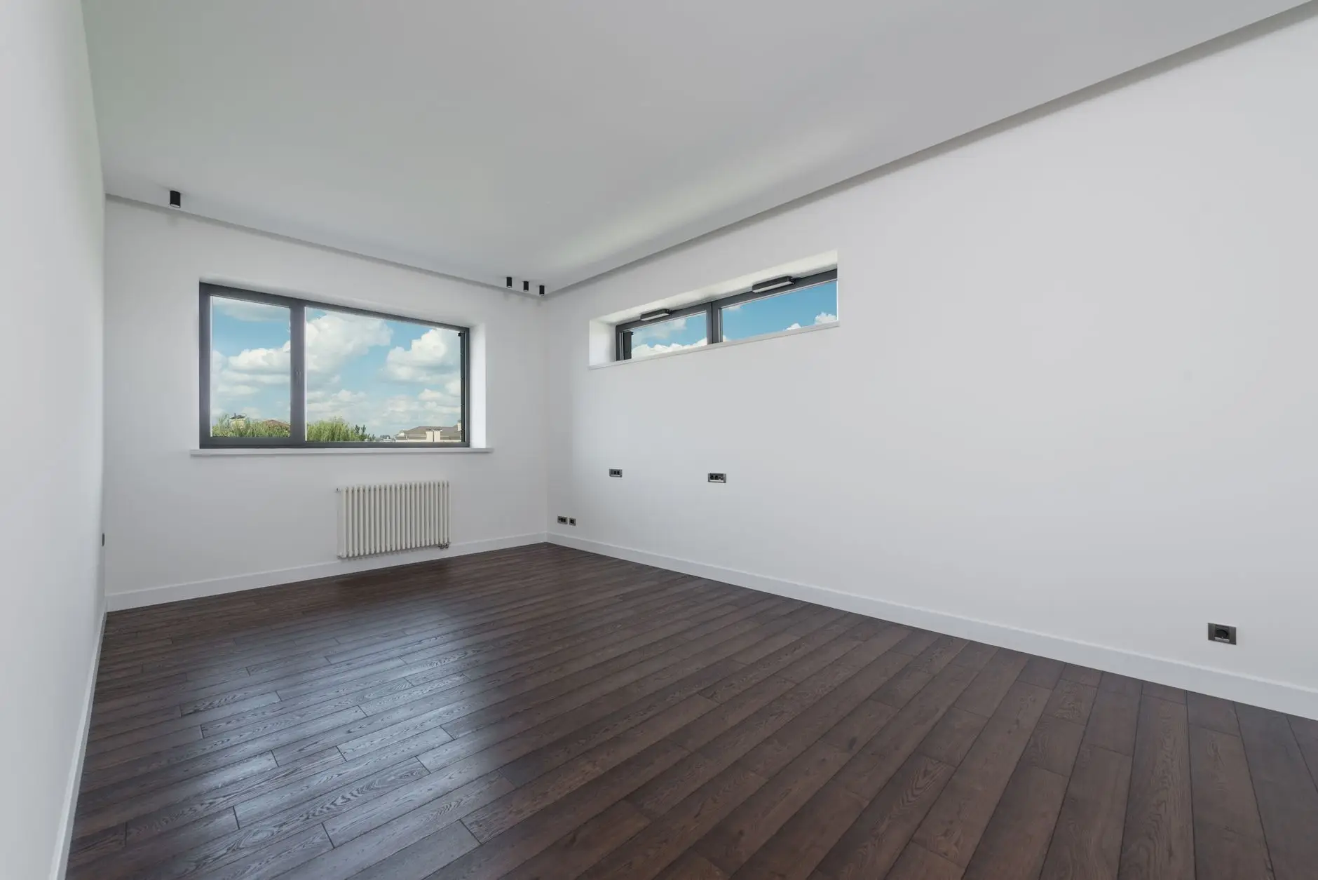 Empty finished room with dark wood-effect flooring, white walls, windows and a radiator
