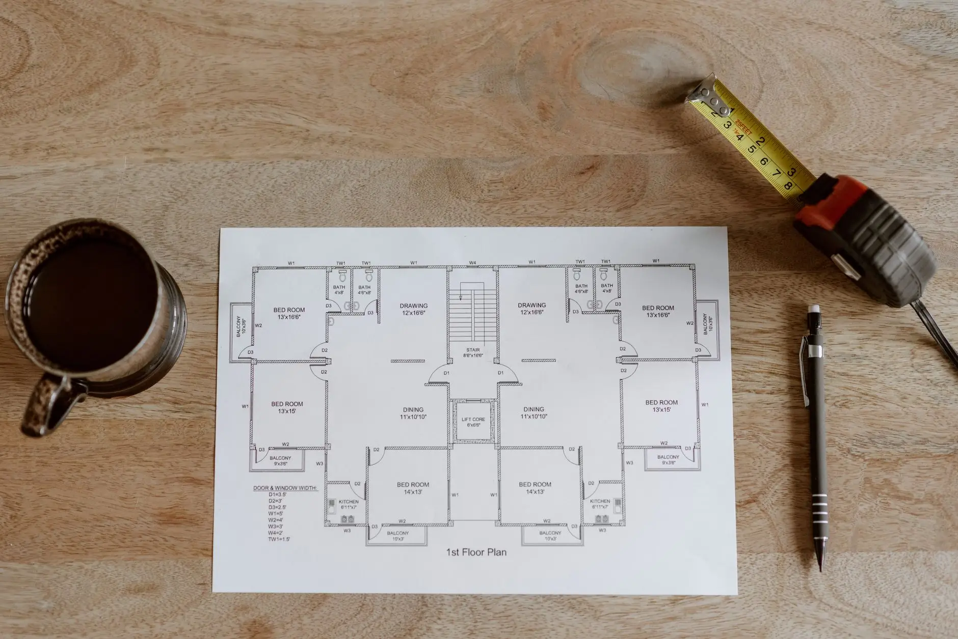Floor plan drawing on a wooden table with a tape measure, pen and coffee