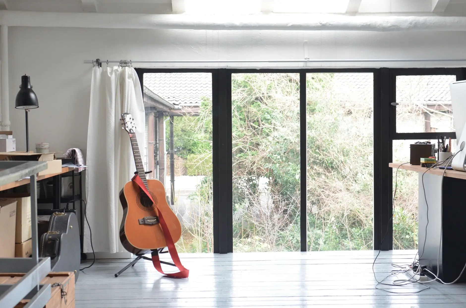 Light-filled studio room with a guitar on a stand and full-height glass doors